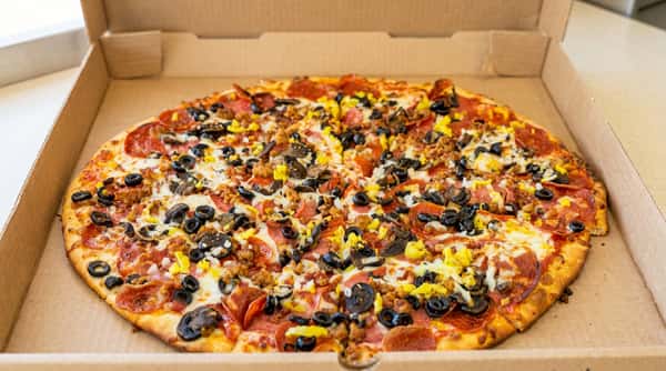 Pizza with pepperoni, sausage, black olives, mushrooms, and yellow peppers in a cardboard box.