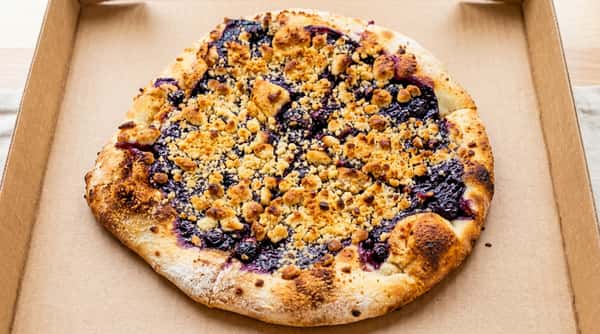 Blueberry crumble dessert pizza with a golden-brown crust, topped with dark blueberries and streusel crumble.