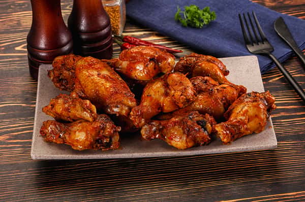 Platter of crispy buffalo chicken wings served on a white plate with seasoning on a wooden table