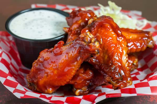 Barbecue chicken wings with glossy sauce served in a red checkered basket with ranch dressing