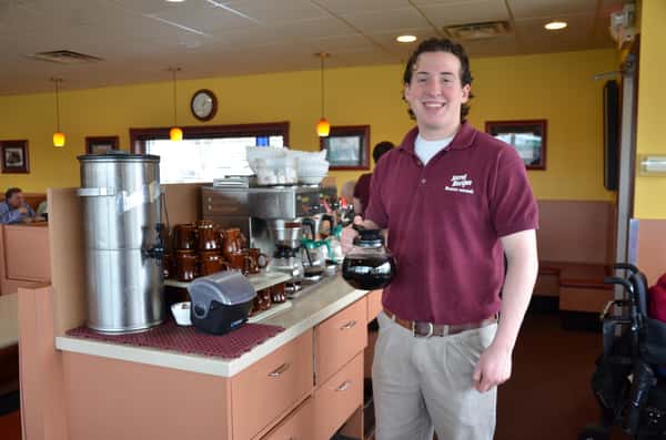 waiter smiling at the camera holding a pot of coffee