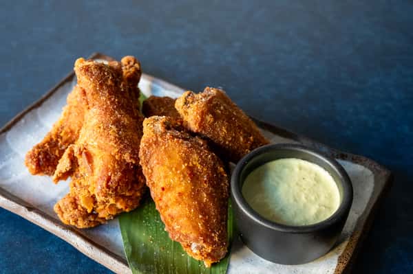 Crispy Japanese fried chicken wings with a creamy dipping sauce, plated on a rustic ceramic dish.