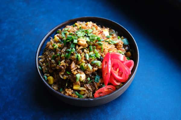 Japanese fried rice with scallions, corn, and pickled ginger, served in a black bowl on a blue table.