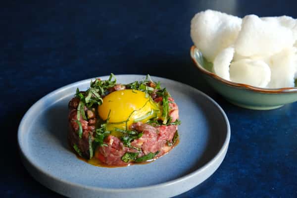 Beef tartare with egg yolk and herbs, paired with puffed rice crackers for a modern izakaya-style appetizer.