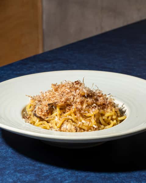 Japanese noodle dish topped with bonito flakes and mushrooms, presented in a minimalist ceramic bowl.