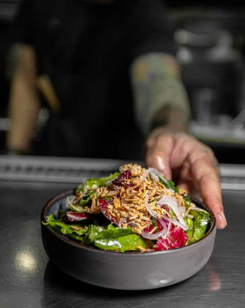 Mixed greens salad with herbs, sliced onion, and crispy topping, presented in a modern Japanese bowl.