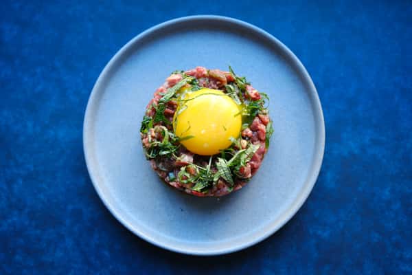 Beef tartare topped with a raw egg yolk and fresh herbs, plated simply for a modern Japanese dining presentation.