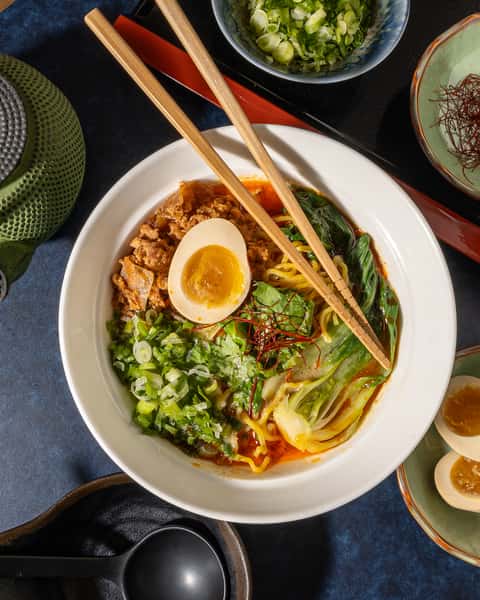 Spicy ramen bowl with minced pork, bok choy, soft-boiled egg, chili oil, and wheat noodles, photographed overhead.