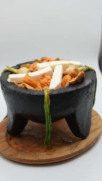 Traditional Mexican molcajete bowl filled with sizzling shrimp, grilled chicken, nopales (cactus), and thick slices of queso fresco, garnished with grilled green onions and served on a wooden board—hearty and flavorful specialty dish served hot.