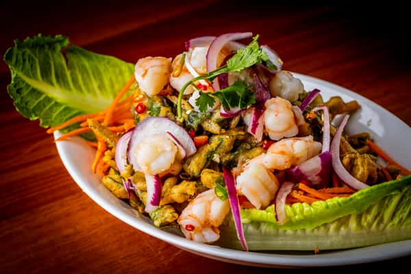 Spicy shrimp salad with herbs, red onion, carrot, and lettuce leaves, garnished with cilantro and chili on a white plate.