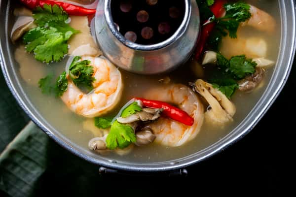 Shrimp hot pot soup with clear broth, red chilies, mushrooms, and fresh cilantro in a metal pot.