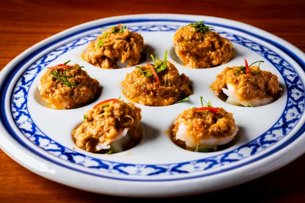 Seven bite-sized dumplings topped with spiced orange-brown sauce and herbs, arranged on a blue-and-white patterned plate
