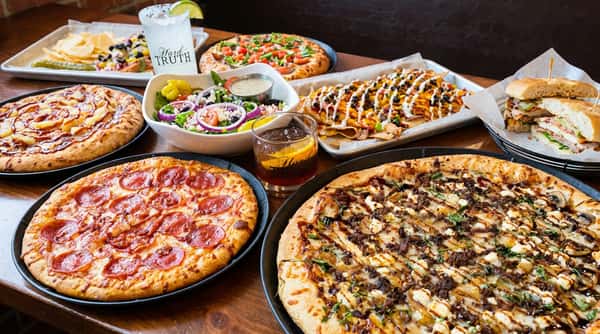 Table spread with four pizzas, a salad, nachos, potato chips, and two drinks.