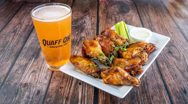 Plate of roasted chicken wings with celery sticks, ranch dip, and a glass of "Quaff On!" beer.