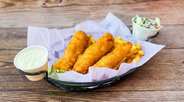 Fish and chips with tartar sauce, served in a black basket on a wooden table.