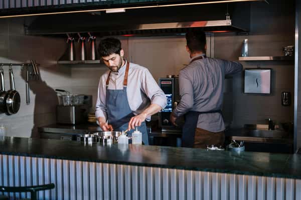 Two chefs are currently preparing food in the kitchen at Pierce Creek, one stirring a pan and the other operating kitchen equipment.