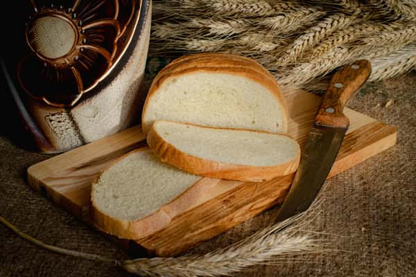 Sliced bread sits on a wooden cutting board alongside wheat stalks and a knife, potentially a freshly baked offering at Pierce Creek.