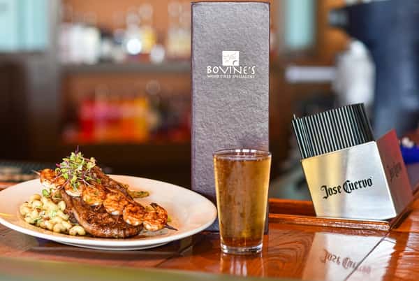 Surf and turf plate with grilled shrimp and steak, served with a cold beer at the bar inside Bovine's, a wood-fired coastal cuisine restaurant in Murrells Inlet, SC.