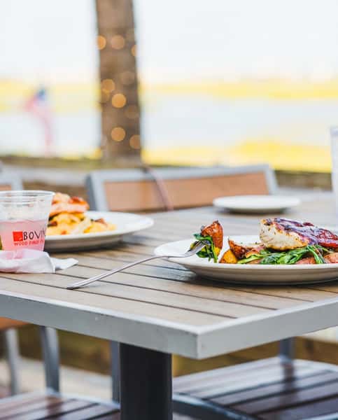 Relaxed waterfront dining at Bovine's in Murrells Inlet, SC, with grilled chicken, sautéed spinach, and roasted potatoes served on the patio overlooking scenic marsh views.