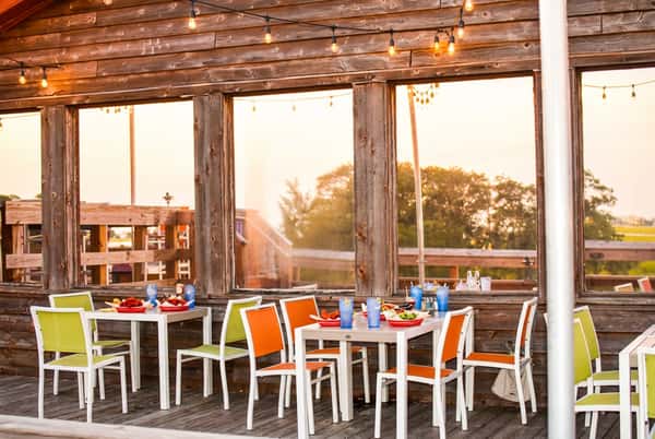 Rustic sunset patio dining setup at Bovine's in Murrells Inlet, SC, with colorful seating, fresh plates of coastal cuisine, and string lights creating a relaxed waterfront atmosphere.