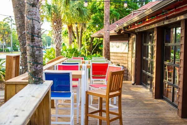 Rustic sunset patio dining setup at Bovine's in Murrells Inlet, SC, with colorful seating, fresh plates of coastal cuisine, and string lights creating a relaxed waterfront atmosphere.