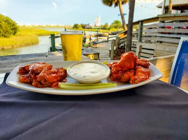 Buffalo chicken wings with celery and ranch dip served dockside at Bovine's in Murrells Inlet, SC, paired with a cold beer and scenic waterfront dining views.
