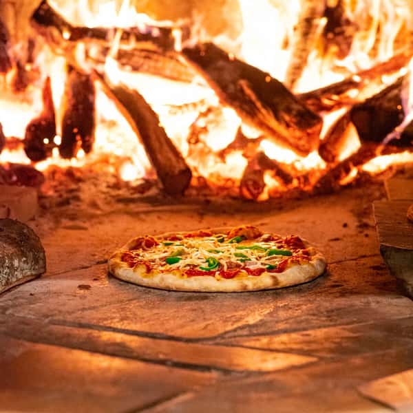 Wood-fired pepperoni pizza baking in a blazing oven at Bovine's in Murrells Inlet, SC, showcasing rustic coastal cuisine with an open flame for bold, smoky flavor.