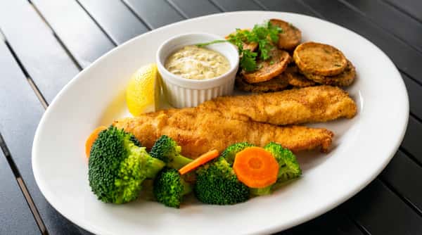 Fried fish fillet with tartar sauce, lemon, broccoli, carrots, and roasted potato slices.