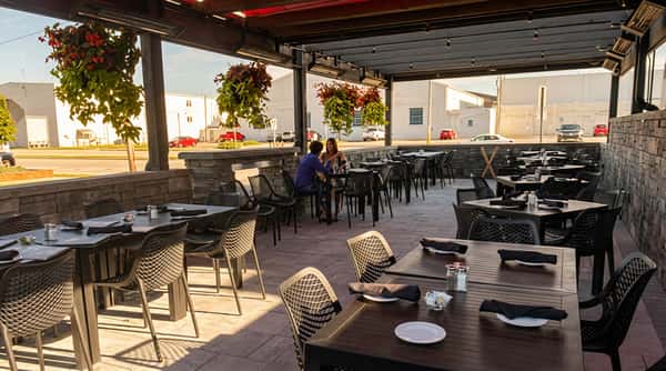 Outdoor restaurant patio with multiple tables and chairs, set under an awning with hanging flower baskets.