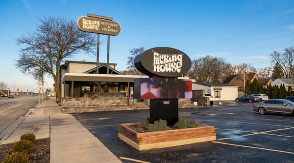 "The Packing House Restaurant & Cocktails" sign next to an electronic marquee displaying "900." A bare tree stands by a sidewalk.