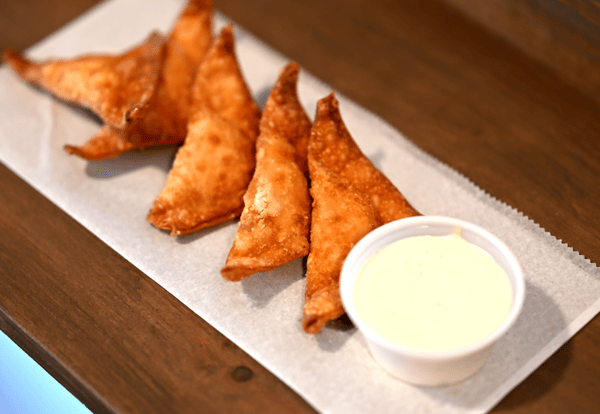 Golden fried wontons arranged on parchment paper, served with a side of creamy dipping sauce in a small cup.