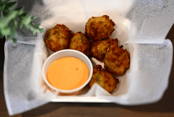 Fried hush puppies served in a paper-lined tray with a side of creamy orange dipping sauce.