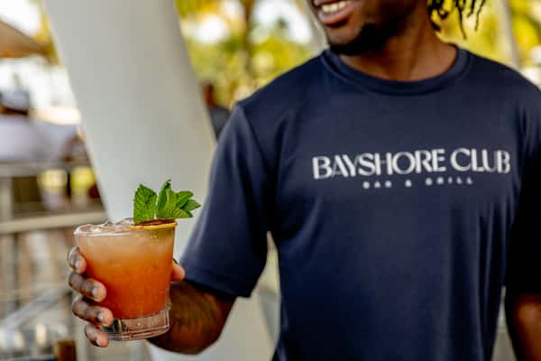 Bayshore Club staff member holding an iced cocktail garnished with mint and dried citrus.