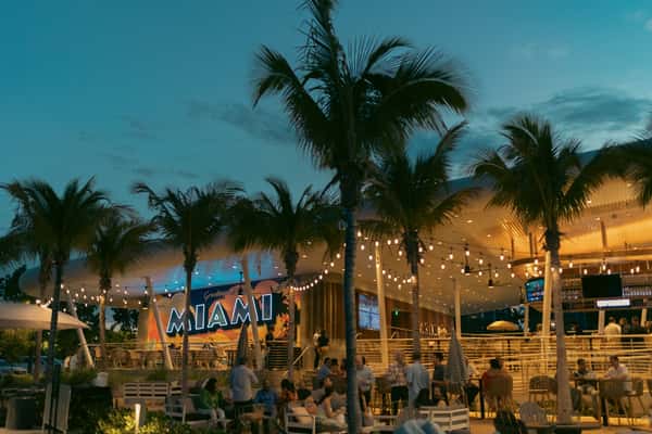 Bayshore Club outdoor restaurant and bar at dusk with palm trees, string lights, and Miami-inspired décor.