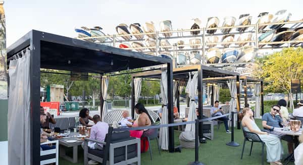 Outdoor cabana-style seating at a Miami waterfront restaurant with boats stacked in the background and guests dining on a sunny afternoon.