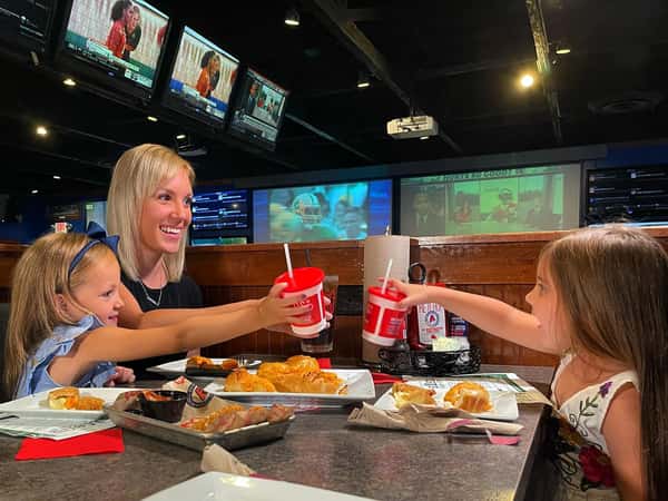 Family savoring drinks and entrees while watching live sports on large screen tvs
