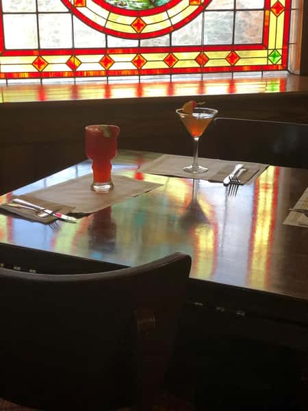 Two cocktails on wooden table in front of stained glass window