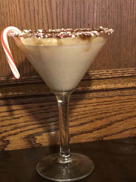 Egg nog cocktail in a martini glass with a candy cane garnish
