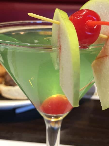 Green cocktail in a martini glass with a lemon wedge and a cherry
