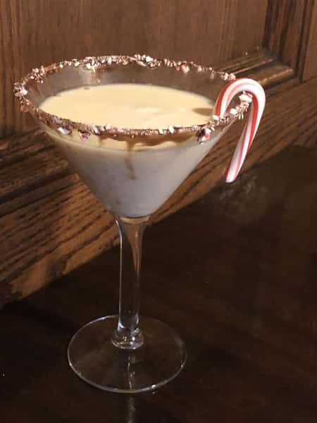 egg nog in a martini glass, rimmed with caramel and crushed candy cane, with candy cane garnsih