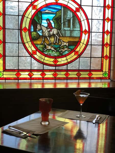 Two cocktails on wooden table in front of stained glass window