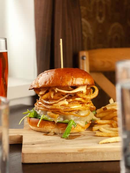 Have you had our Blooming Onion 50/50 Burger yet? Our 1/2 beef, 1/2 bacon patty topped with cheddar, arugula, crispy onions, pickle, and Sriracha ranch, on a brioche bun, with shoestring fries. #BurgerOfTheDay