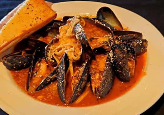 The third image displays a seafood entrée filled with mussels and shellfish in a savory broth, served with toasted bread for dipping.