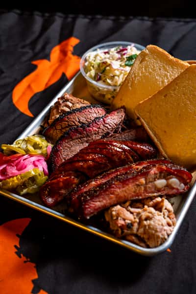 BBQ platter with pulled pork, ribs and sliced brisket served with a side of potato salad and two slices of bread