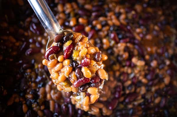 A spoon scooping up a serving of baked beans from a catered pan