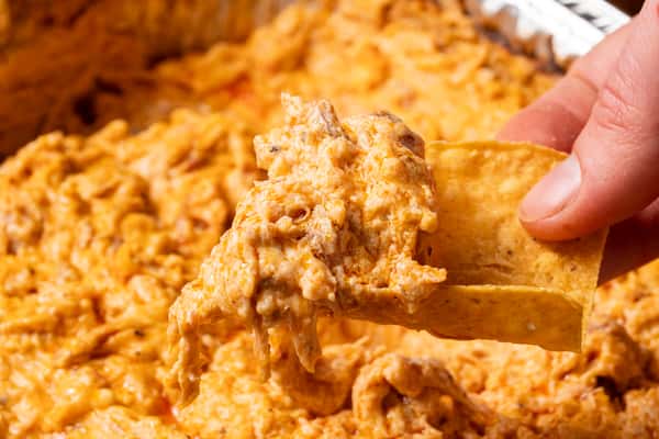 A hand holding a tortilla chip with buffalo chicken dip