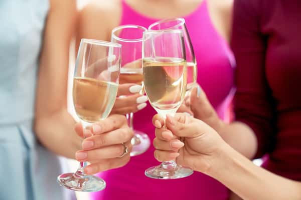 Close up of incognito four girls in colorful dresses celebrating bachelorette party of bride. Hen party before wedding. Gemale friends clinking glasses of champagne. Concept of party, wedding.
