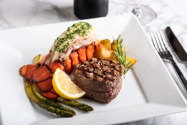 Grilled filet mignon, lobster tail, lemon wedge, asparagus on a square white plate