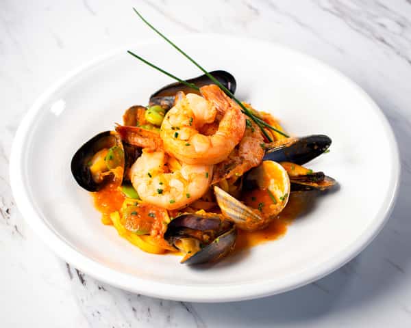 shrimp and mussels served in a tomato broth on a white plate on a white background