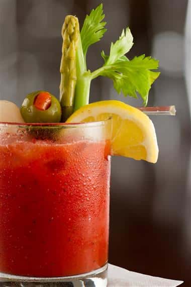 bloody mary cocktail isolated on a busy bar top garnished with onions, olives, asparagus and celery